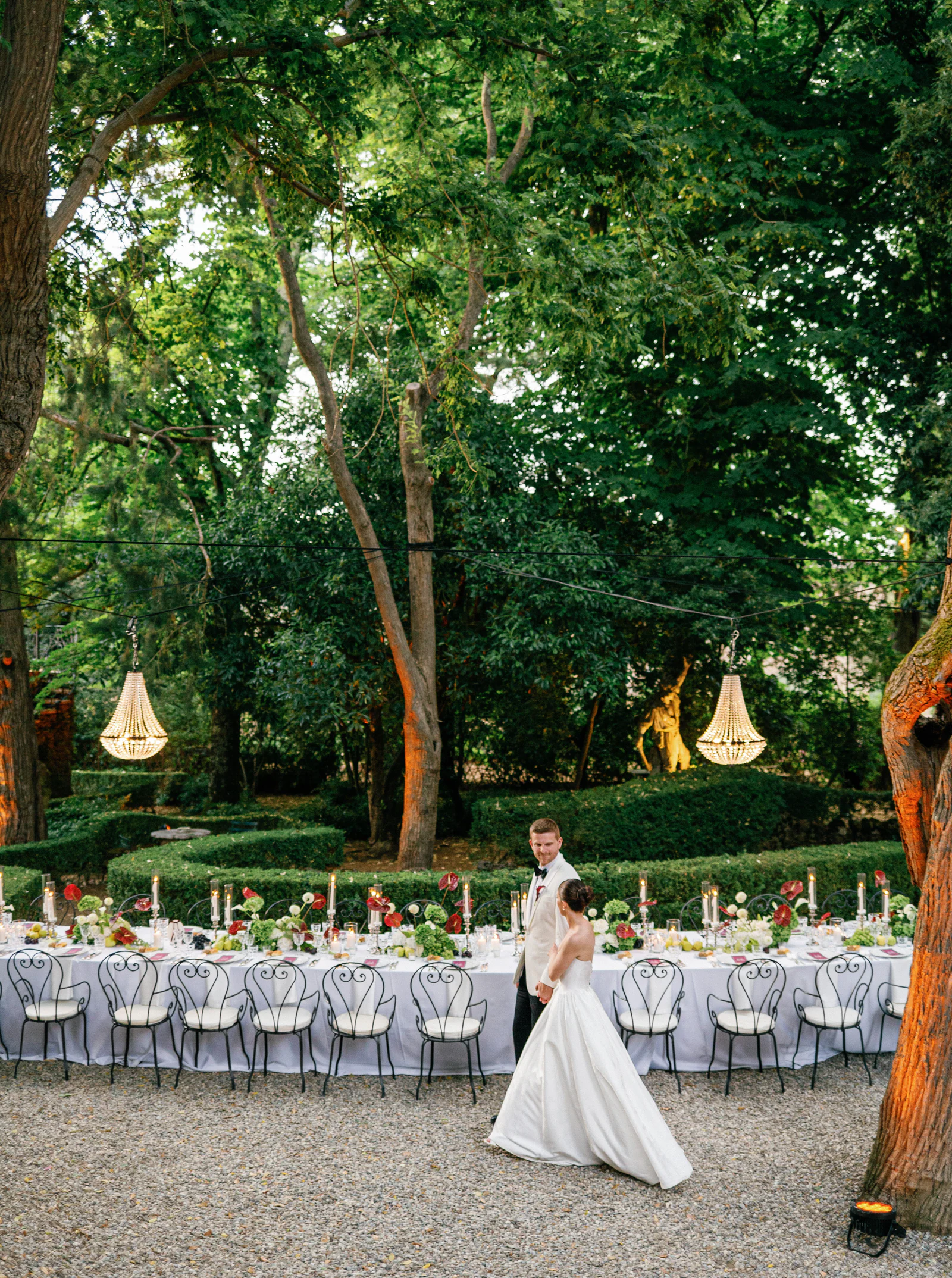 The bride walking past the long dinner tables in the wooded garden of Borgo Stomennano, Chianti, Tuscany